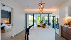 Una habitación de hotel moderna con una cama grande, un área de comedor con vistas al jardín y una cocina con encimera de mármol.