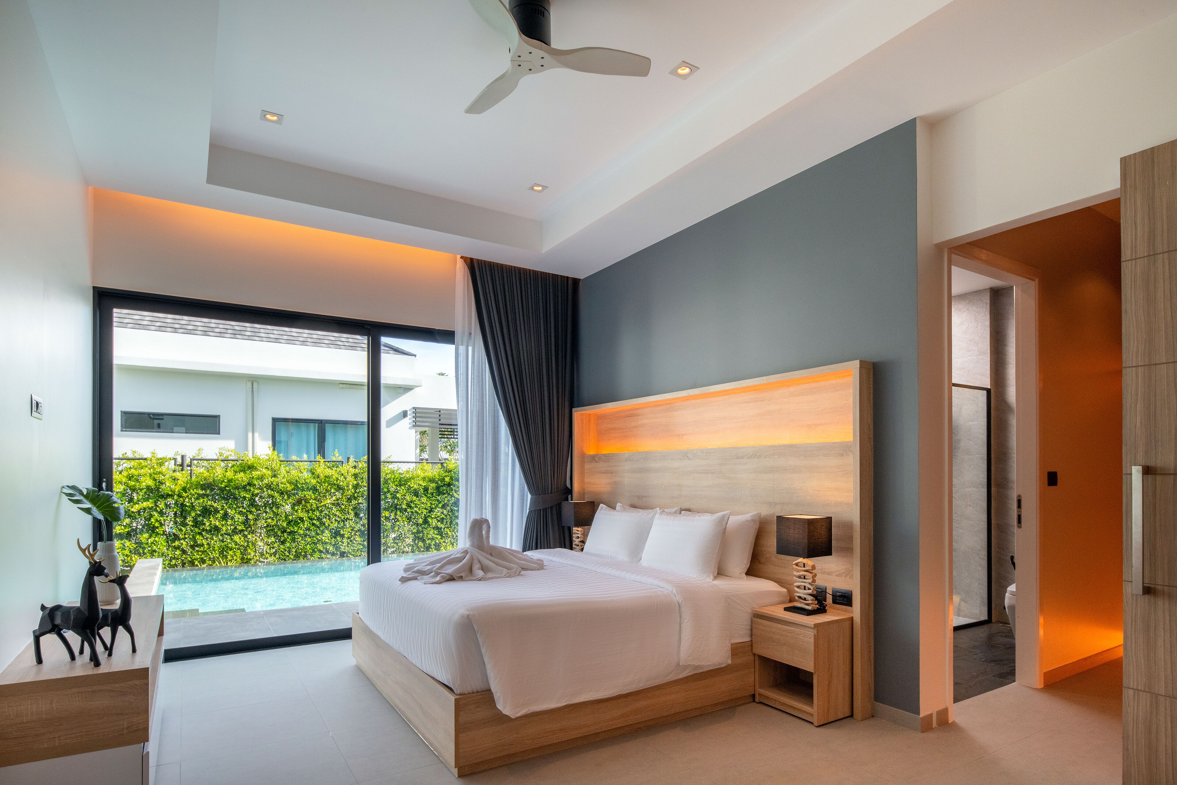 Ein modernes Hotelzimmer mit einem großen Bett, Nachttischen, einem Deckenventilator und Blick auf einen Swimmingpool.