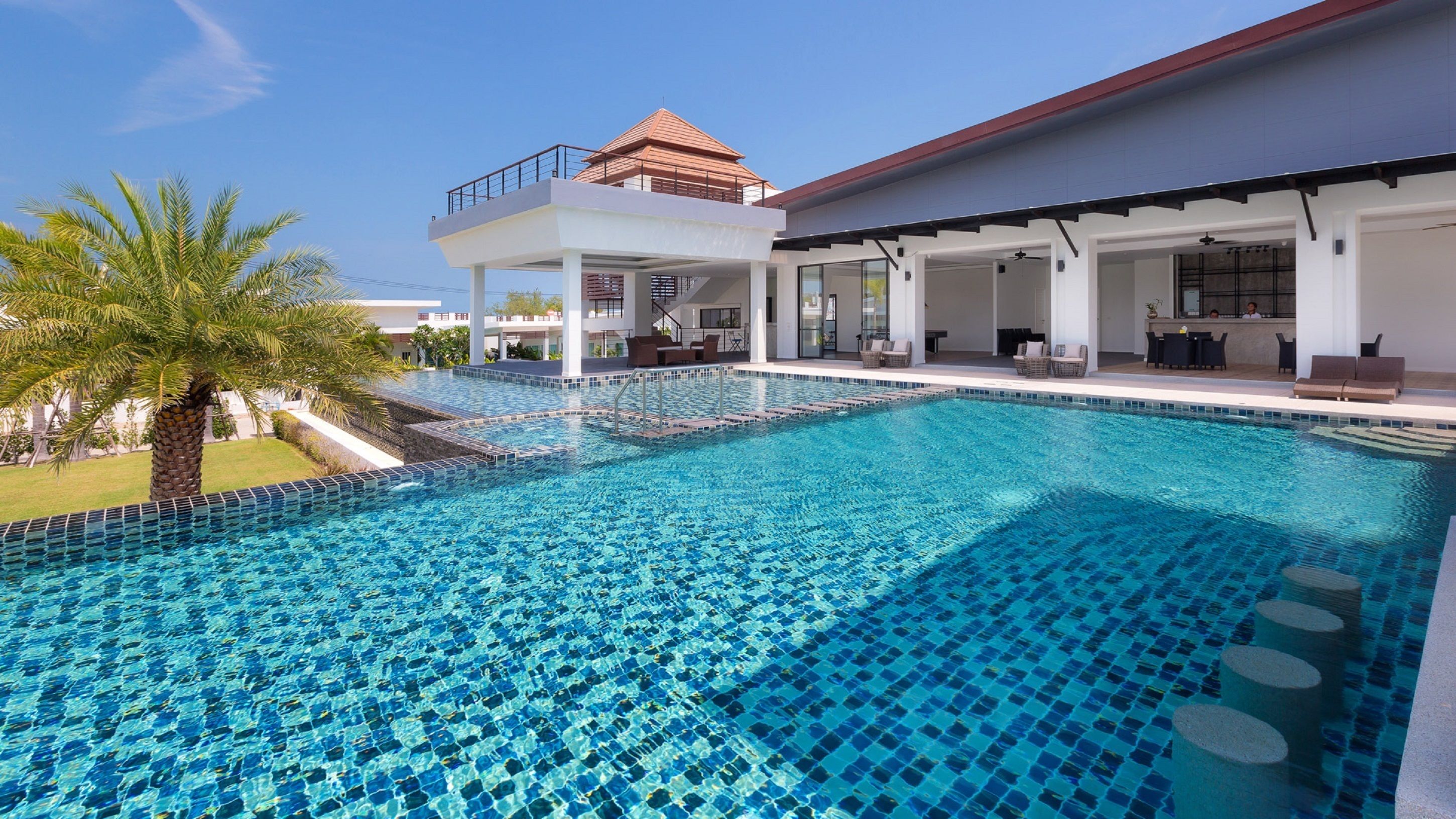 A swimming pool with a tiled deck and a covered outdoor seating area.