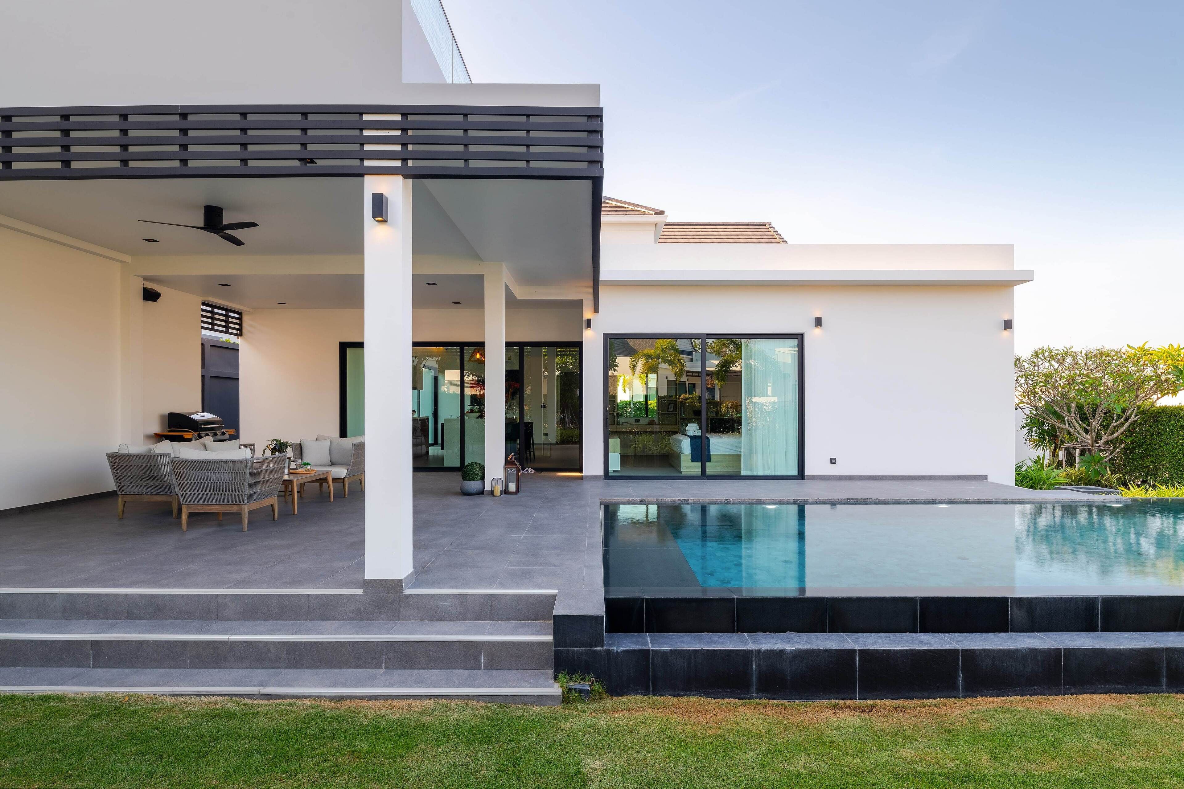 Ein modernes Haus mit Pool, Sitzgelegenheiten im Freien und einer überdachten Terrasse.