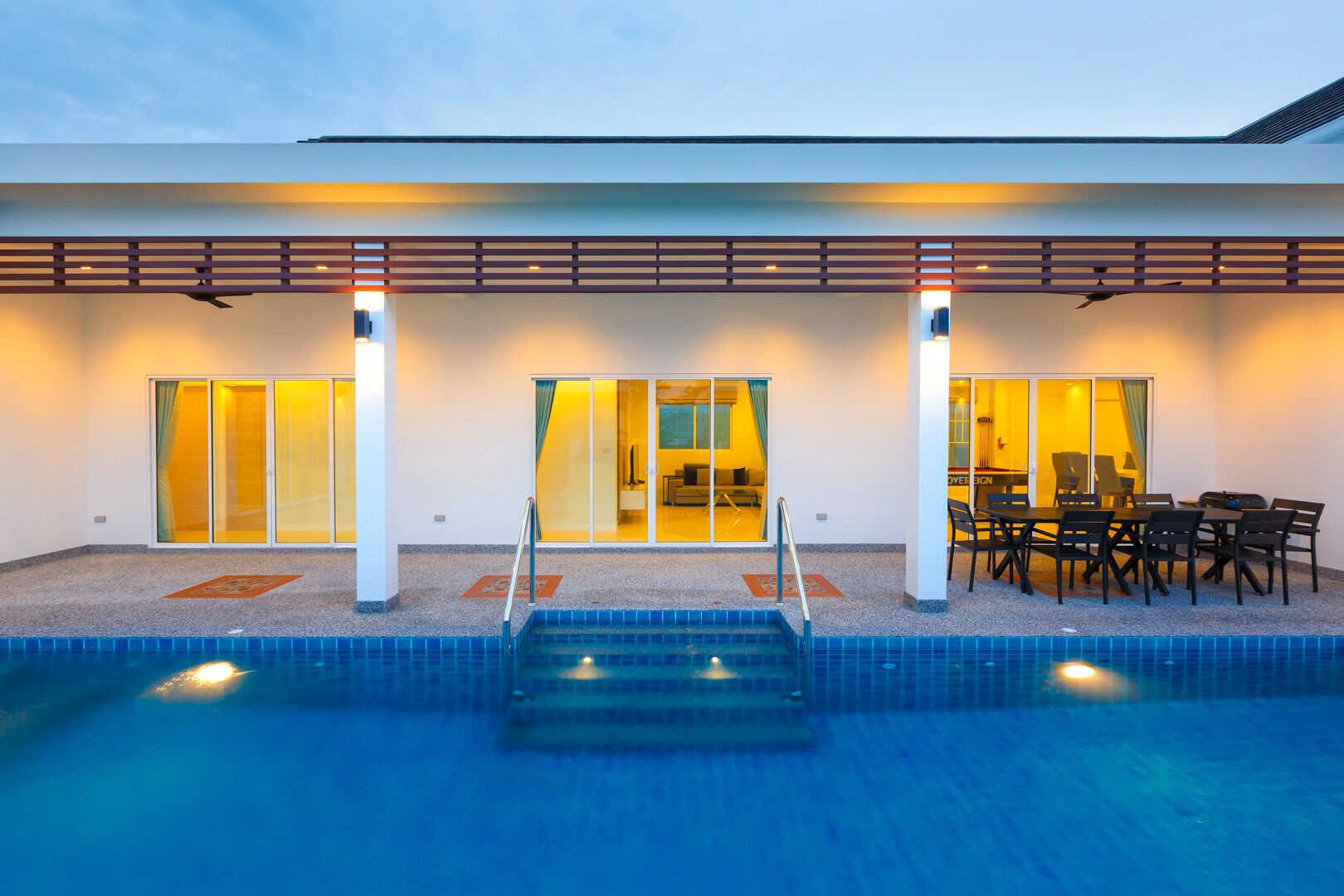 A modern hotel with a swimming pool, large sliding glass doors, and a patio area with outdoor seating.