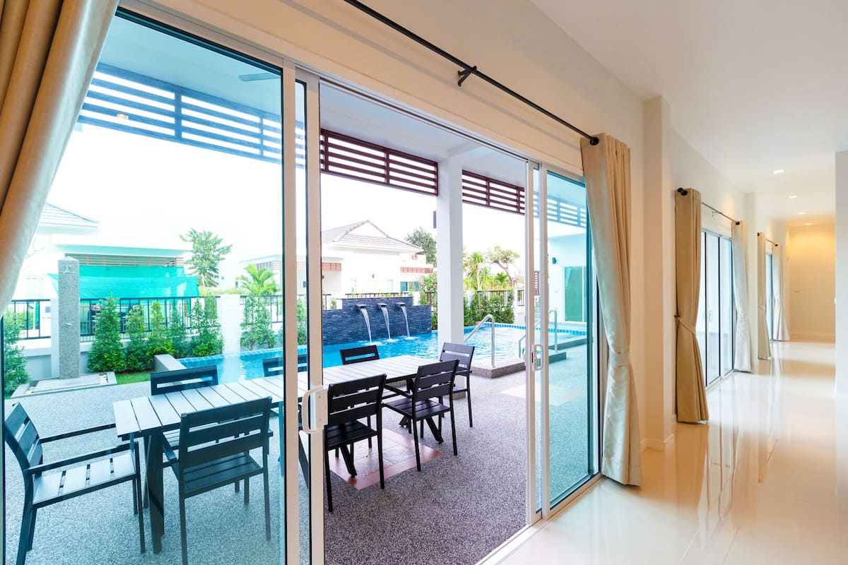 Una habitación de hotel moderna con puerta de vidrio que da a una zona de piscina, mobiliario exterior y vistas a un complejo turístico.