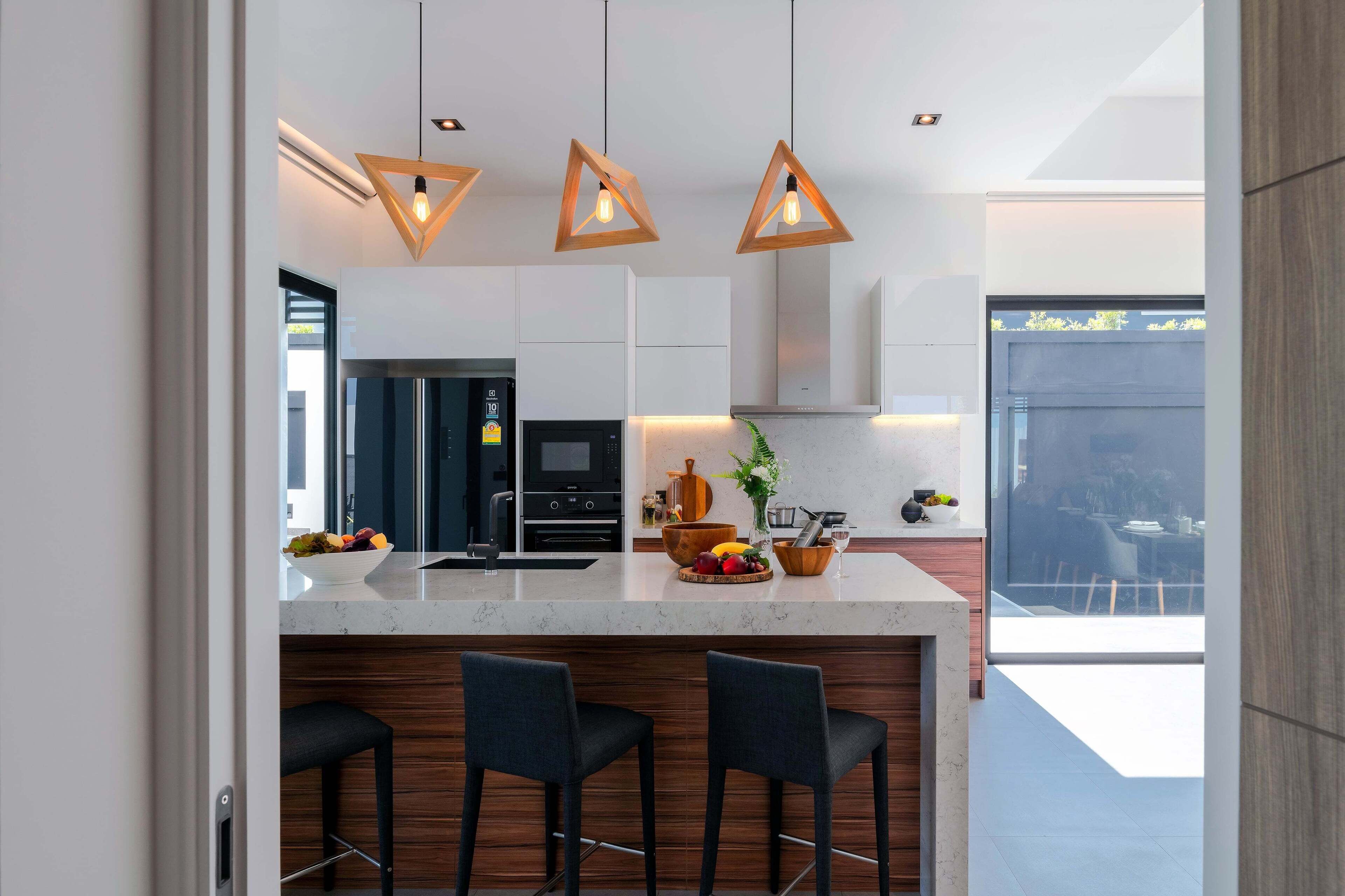 Cozinha moderna com bancada de mármore, banquetes de madeira e iluminação pendente.