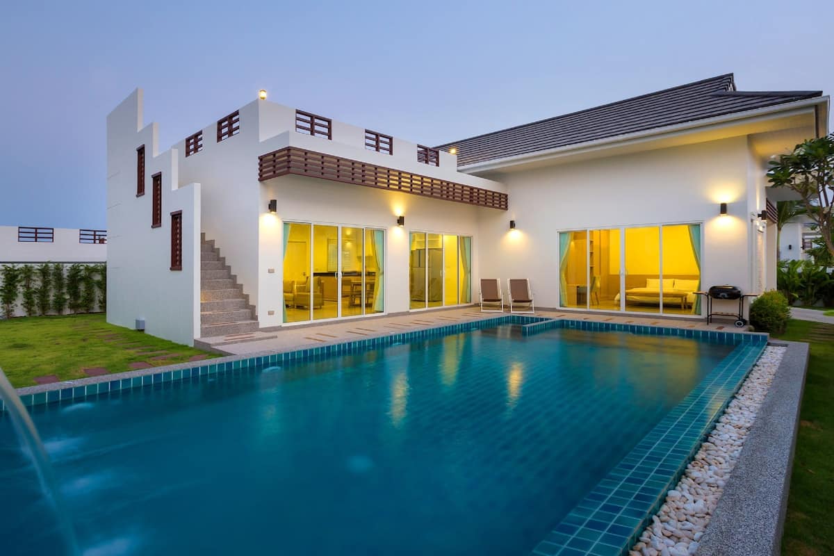 Una casa moderna con piscina, una escalera que lleva a un balcón y un césped bien cuidado.