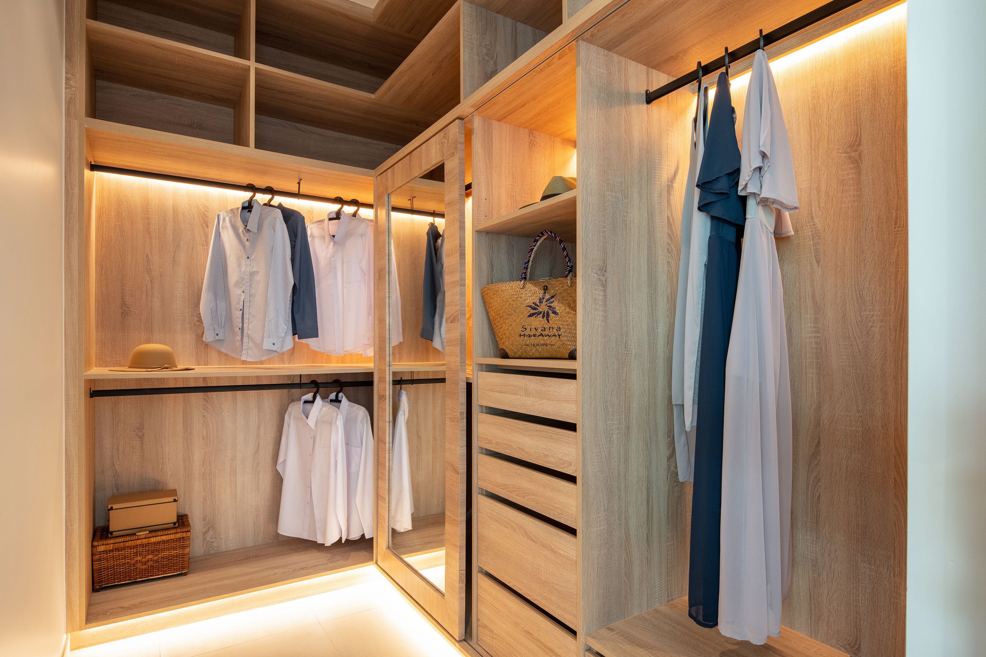 A walk-in closet with wooden shelving and hanging space, featuring neatly organized clothing and storage boxes.