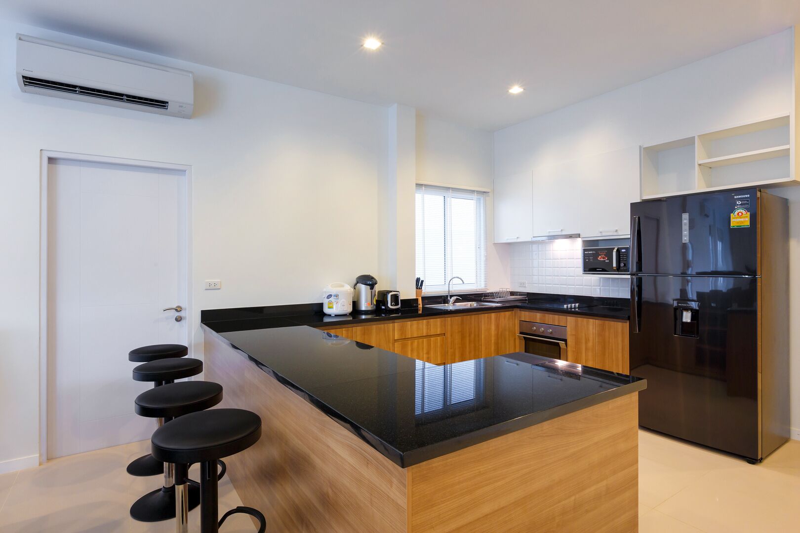 A modern kitchen with a black countertop, wooden cabinets, a stainless steel refrigerator, and a built-in oven.