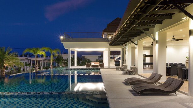 Una piscina infinita con un espacio de estar moderno al aire libre, un patio cubierto y vistas de los edificios circundantes.