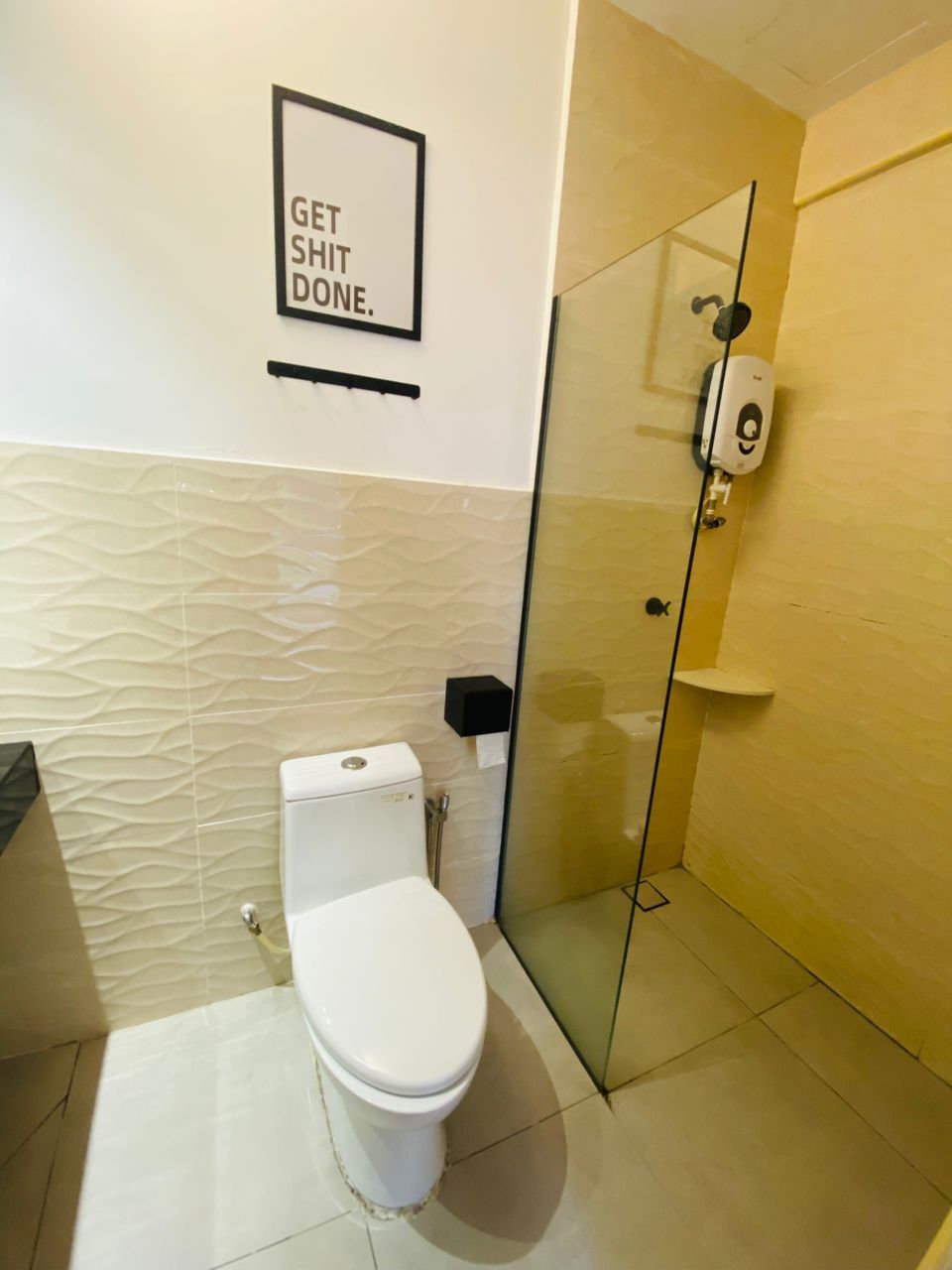 A bathroom with a toilet, a glass shower enclosure, and a framed motivational quote on the wall.