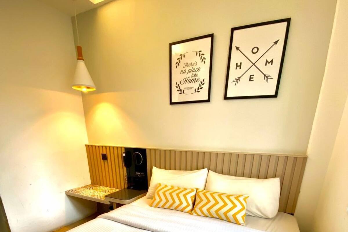 A neatly made bed with white bedding and two decorative pillows, a bedside table with a lamp, and two framed wall art pieces.