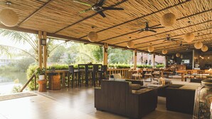 Un espace extérieur aménagé avec des meubles en bois, un toit de chaume et des luminaires sphériques suspendus.