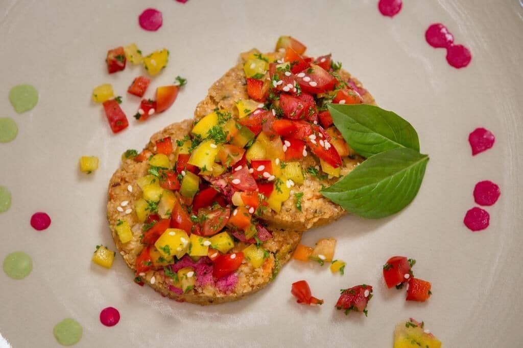 A plate with a food item topped with diced vegetables and a basil leaf.
