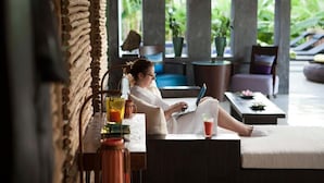 Une personne se détend sur un canapé, un ordinateur portable à portée de main, une boisson sur la table, et une vue sur la verdure à l’extérieur.