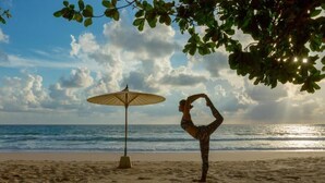 Une scène de plage avec une personne pratiquant une posture de yoga, un parasol de plage et l’océan en arrière-plan.