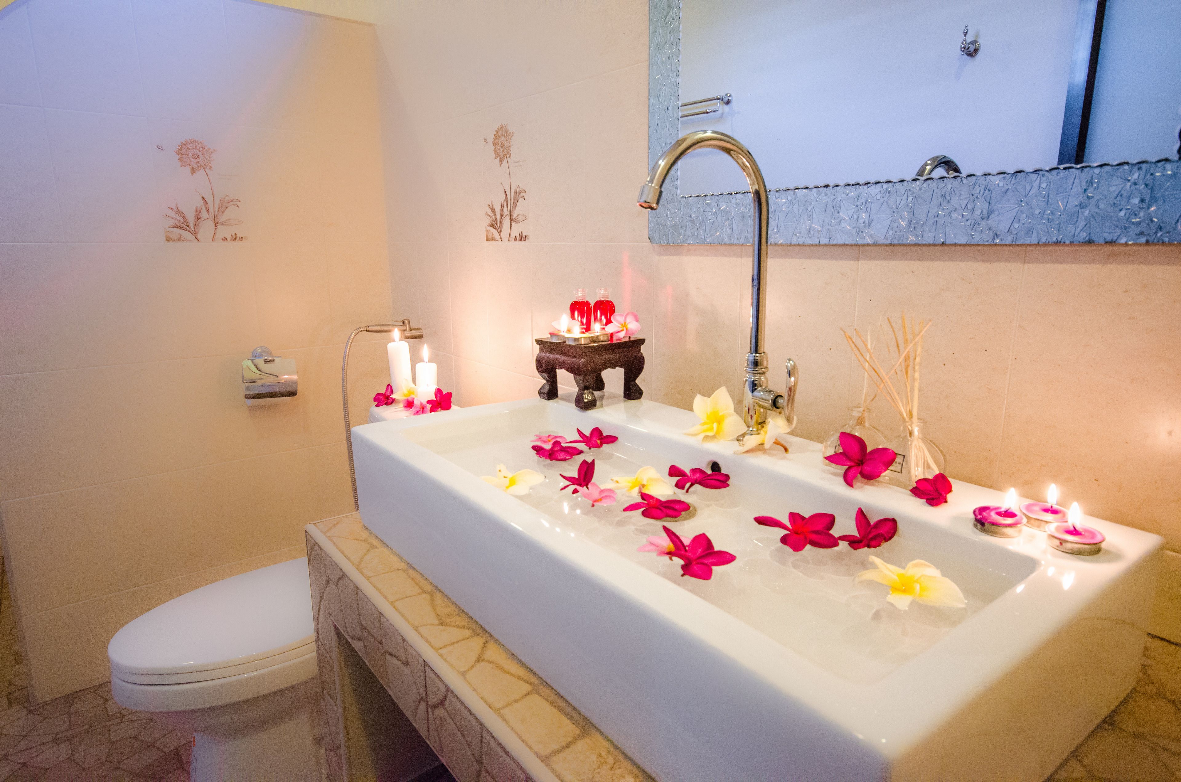 Een badkamer met een groot bad, een toilet en een klein tafeltje met kaarsen en bloemen.