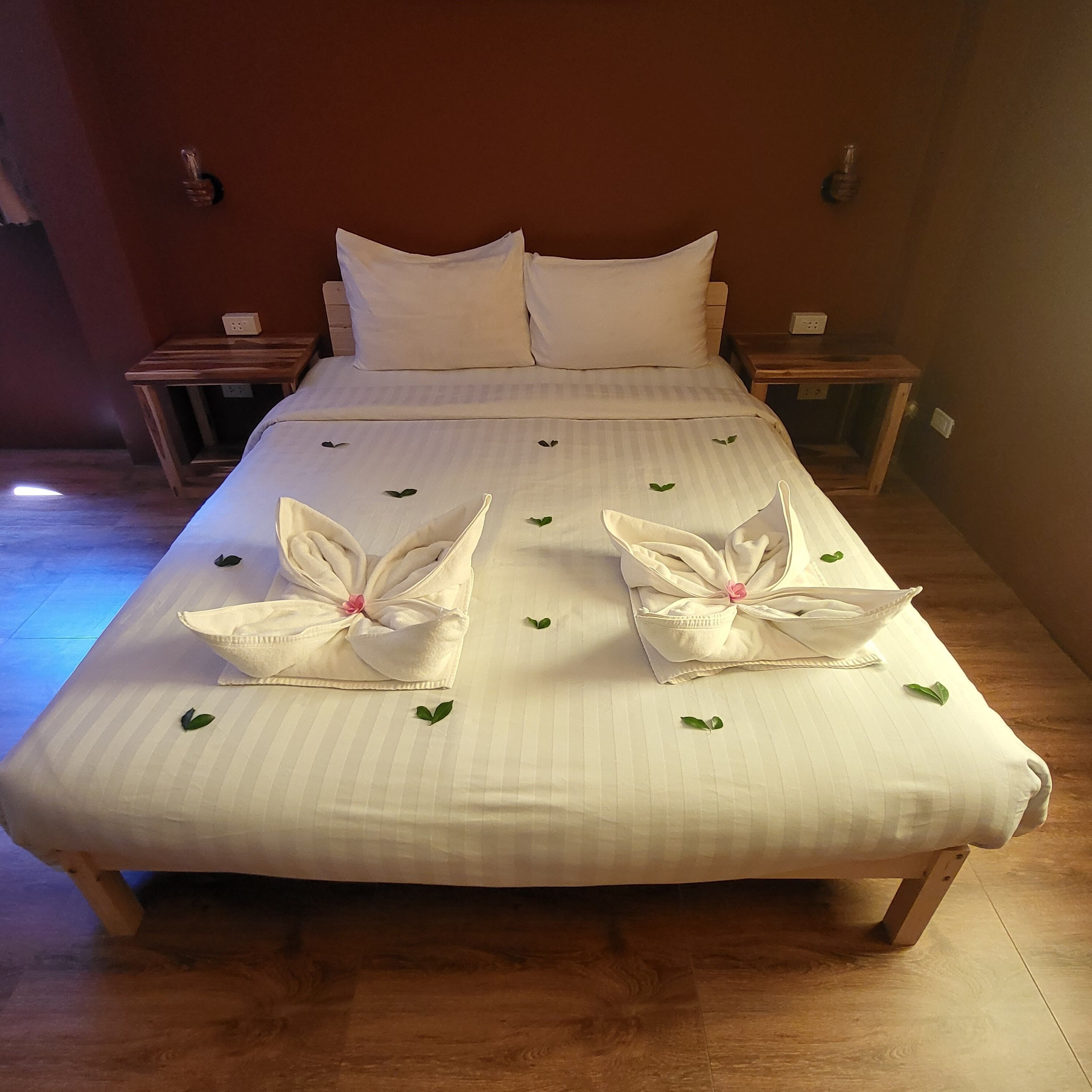 A neatly made bed with a striped bedspread, two pillows, and two towels arranged in a floral pattern.