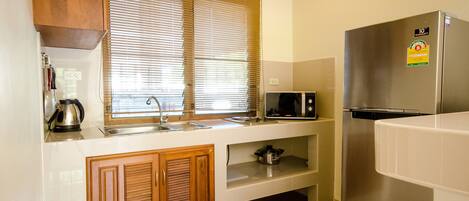 Una cocina moderna con armarios de madera, un refrigerador de acero inoxidable, un microondas y una tetera.