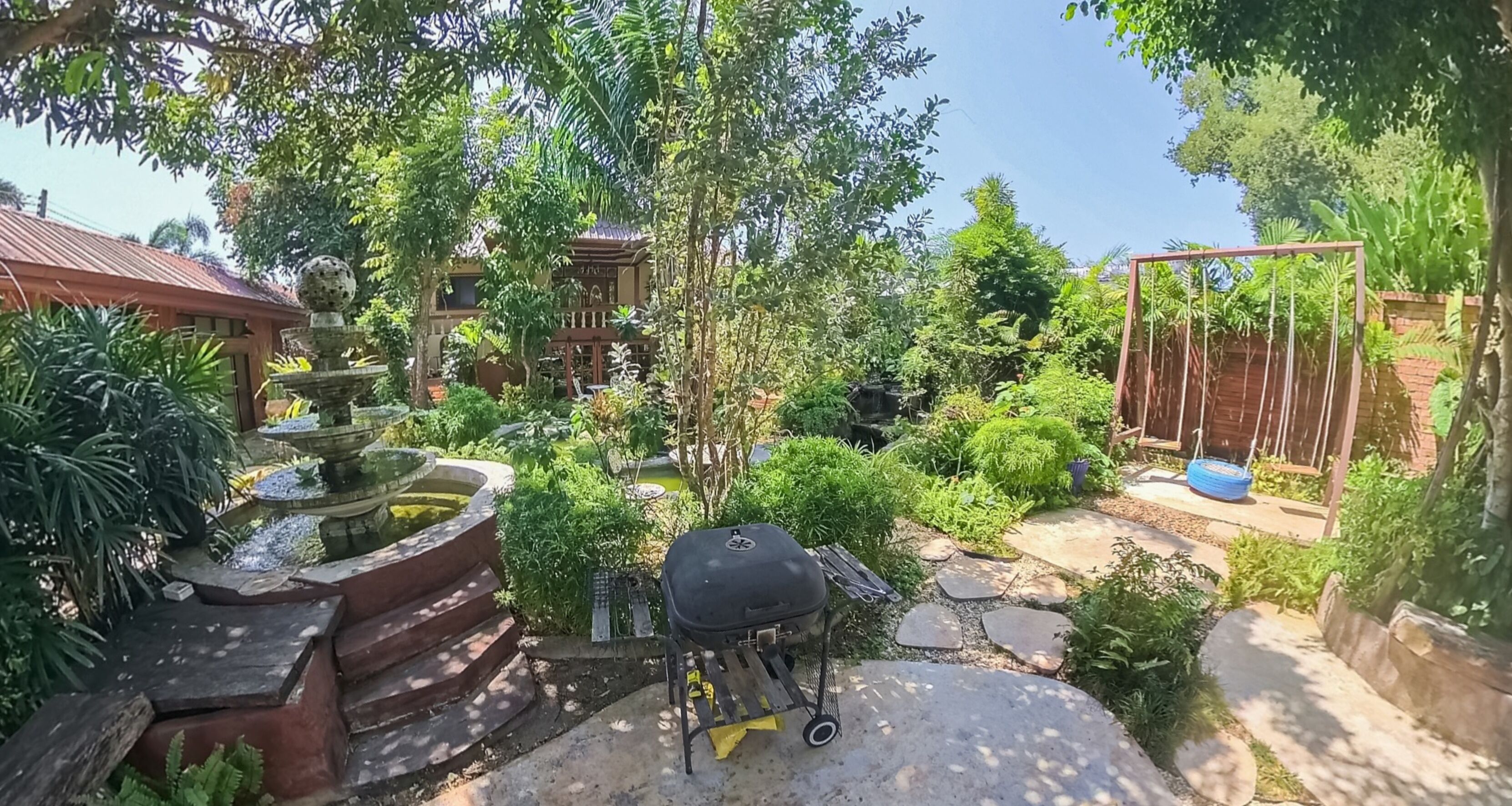 A garden with a fountain, a barbecue grill, and a swing set.