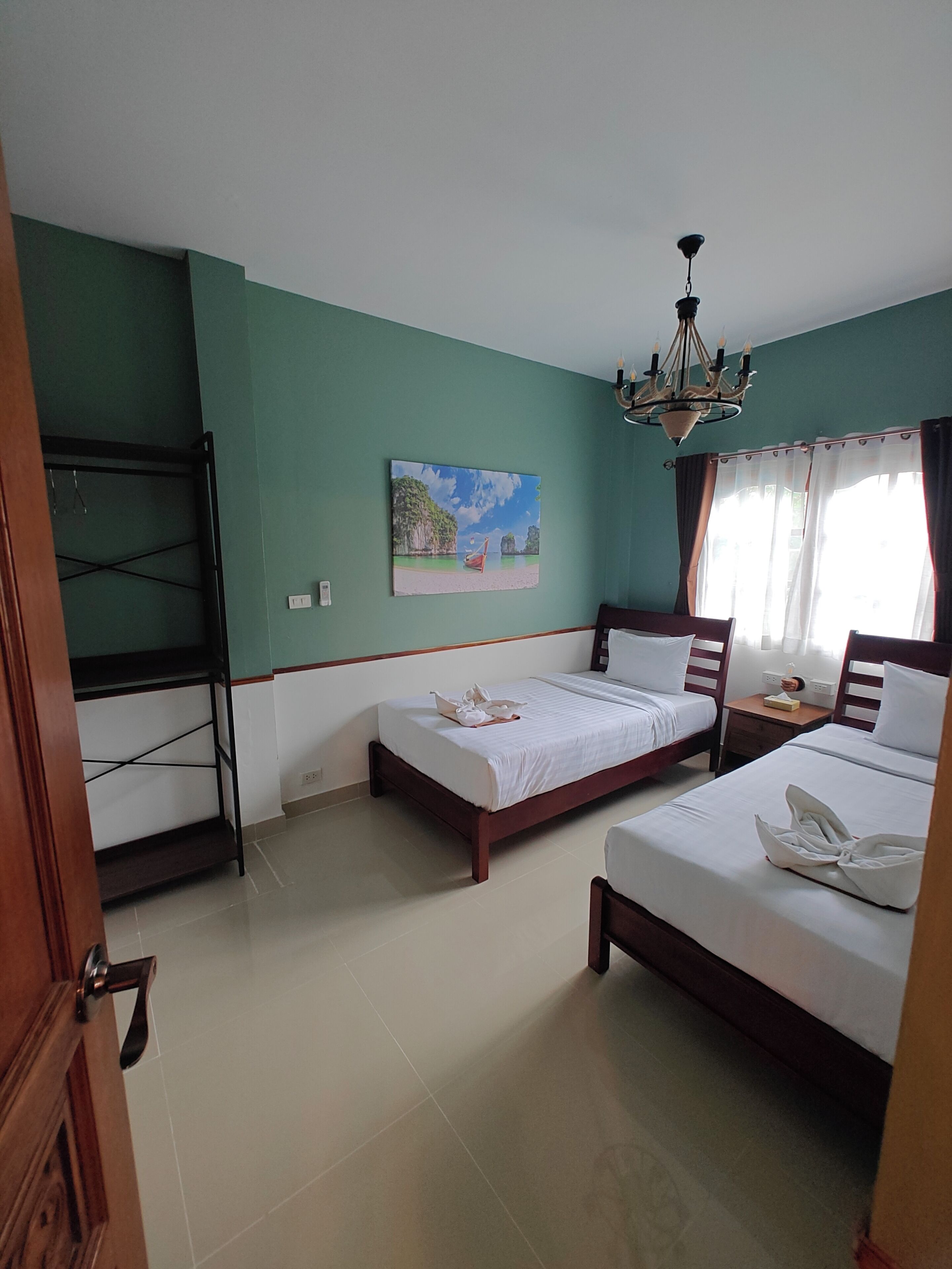 A hotel room with two beds, a painting on the wall, a chandelier, and a view of the outdoors through the window.