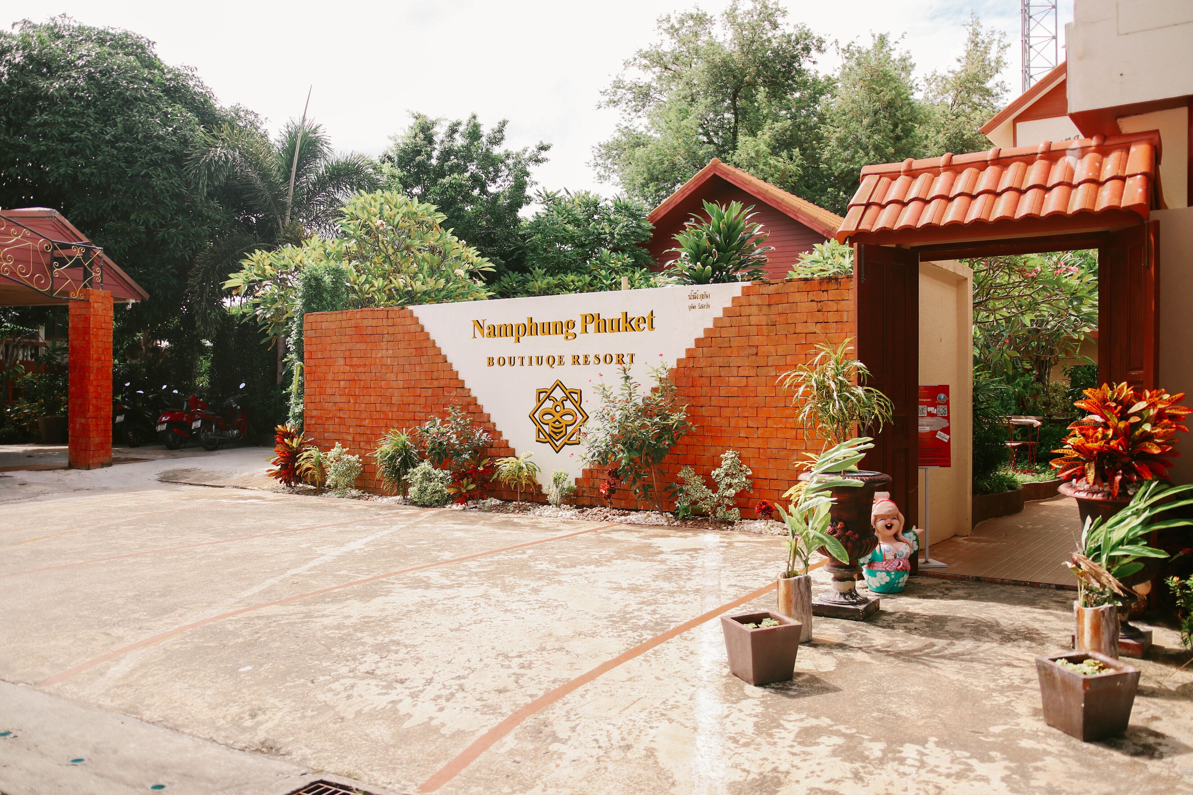 The entrance to Namphung Phuket Boutique Resort with a brick wall, potted plants, and a tiled roof.