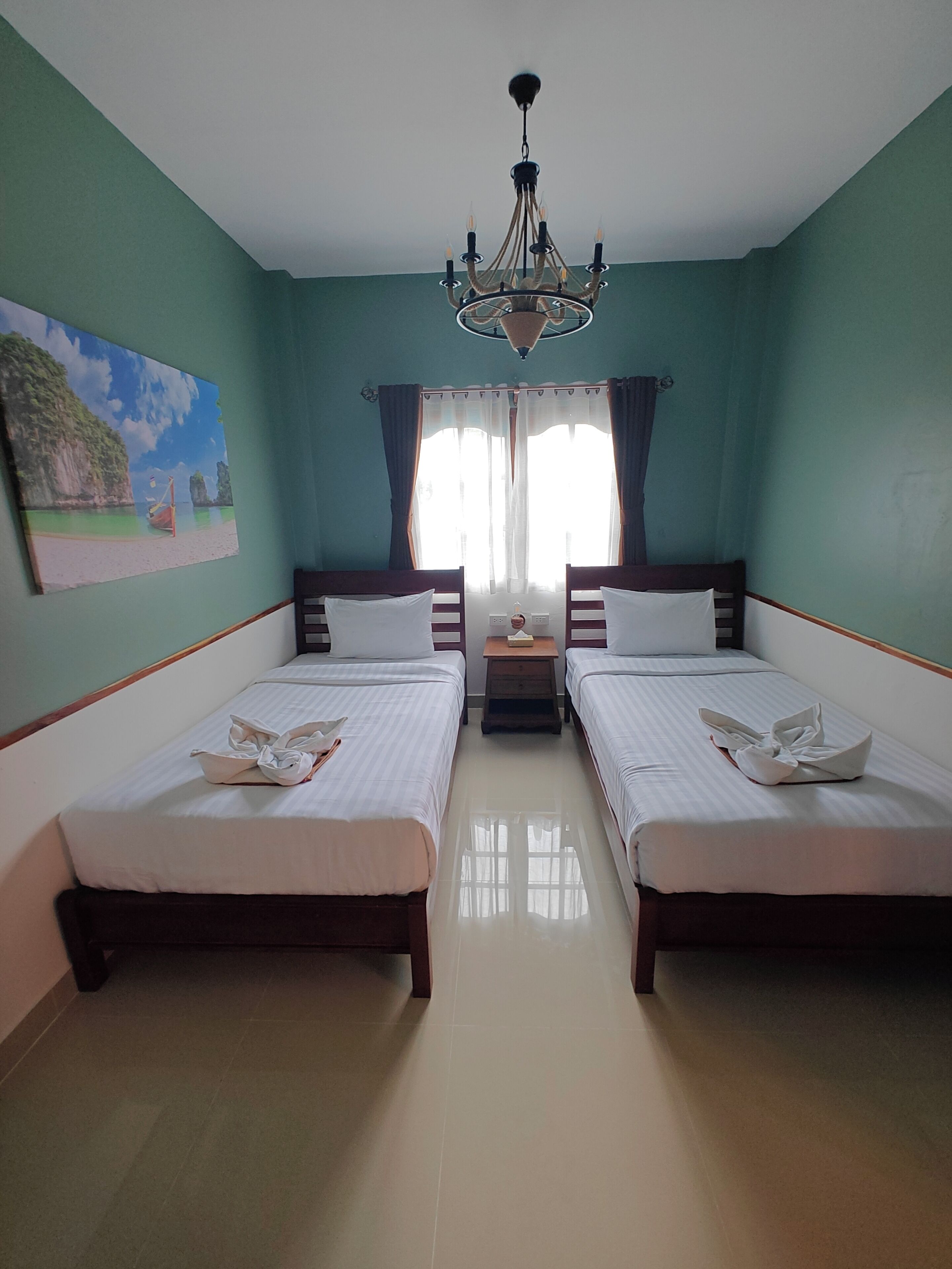 A hotel room with two beds, a chandelier, a painting, and a window with curtains.