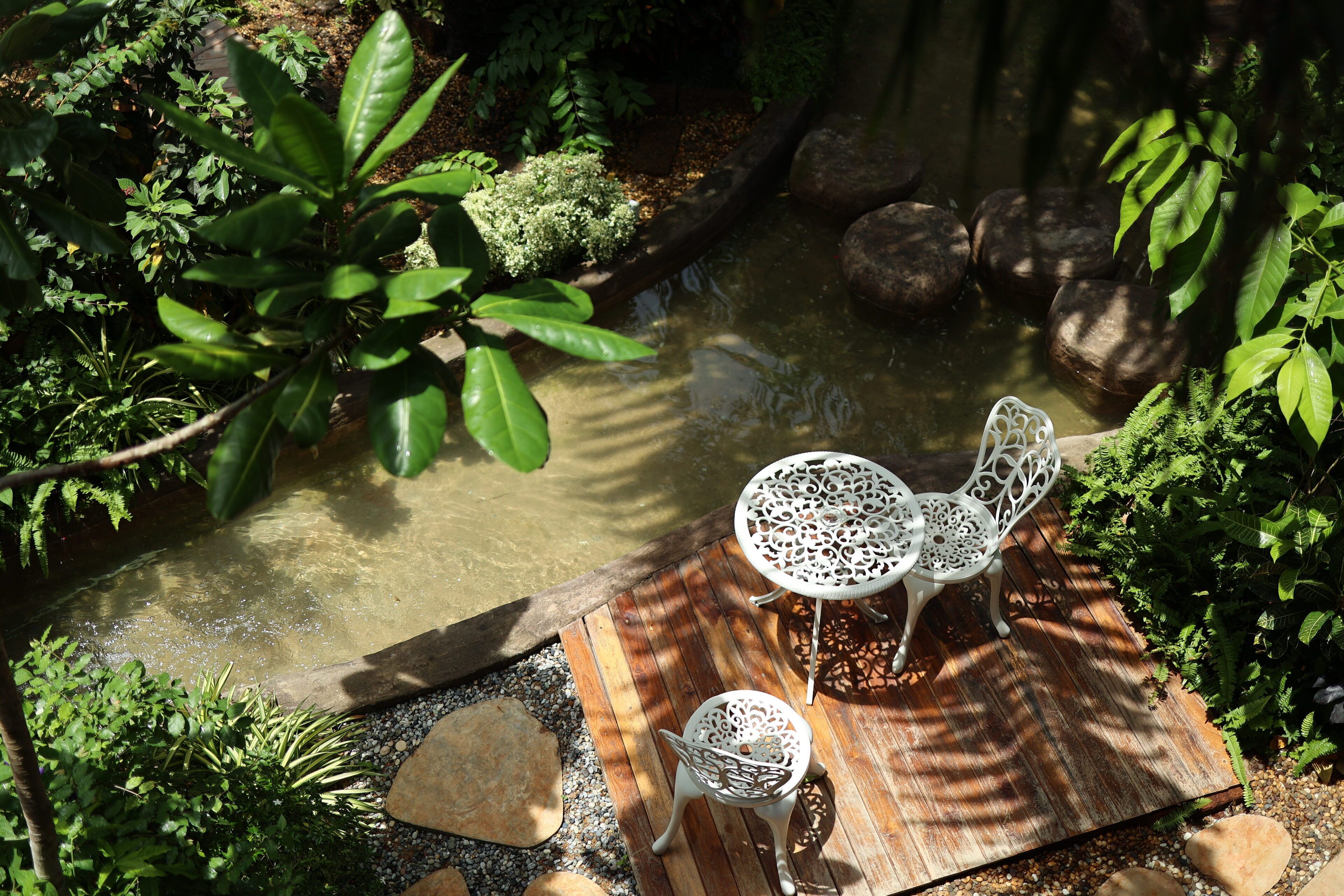 A garden with a pond, two white metal chairs, and a wooden deck.