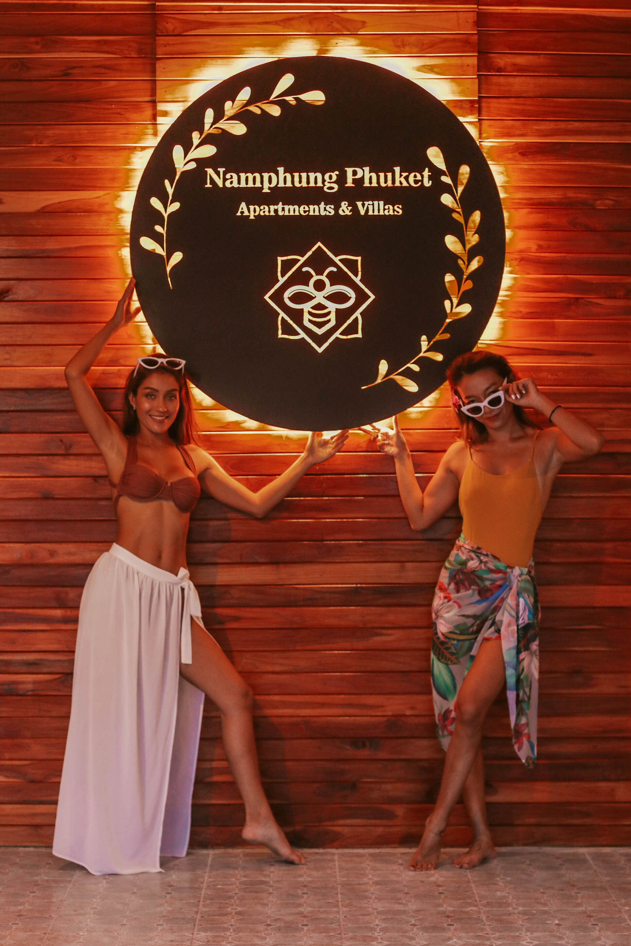 A wooden wall with a circular sign that reads "Namphung Phuket Apartments & Villas".