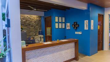 A reception desk with a stone wall backdrop, framed certificates on the wall, and a wooden ceiling fan.