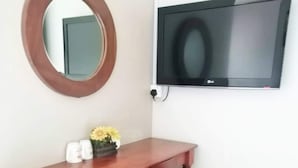 A wooden desk with a chair, a round mirror, and a flat-screen TV mounted on the wall. - John's Place (Kuching)