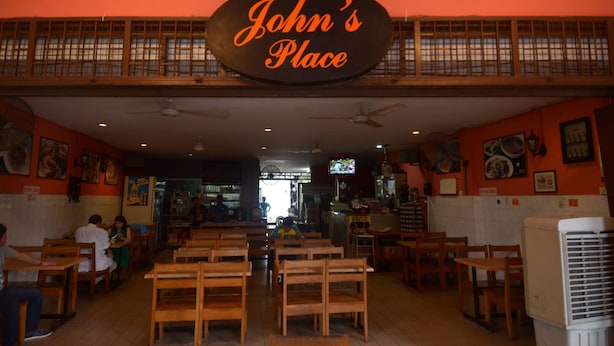 A restaurant interior with a sign reading "John's Place" above the seating area. - John's Place (Kuching)