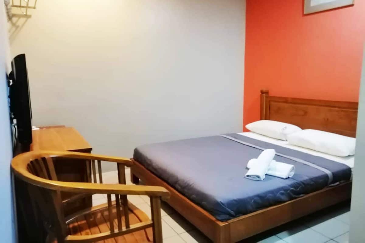 A hotel room with a bed, a wooden chair, a desk, and a television.