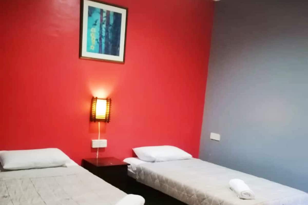 A hotel room with two beds, a red wall, a painting, and a wall-mounted lamp.