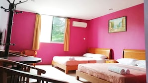 A room with two beds, a desk, and a chair. There is a window with curtains, an air conditioning unit, and a painting on the wall. - John's Place (Kuching)