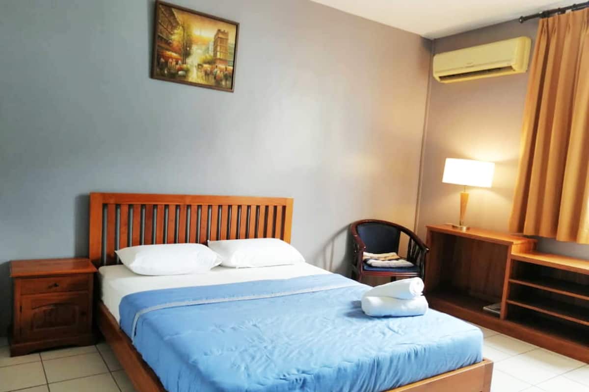 A neatly arranged hotel room with a bed, a chair, a desk, and a lamp.
