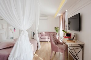 Un dormitorio con cama a dosel, un sofá rosa, un escritorio con una computadora portátil y un televisor en la pared.