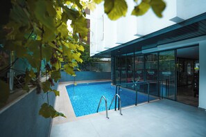 Una piscina interior con paredes de vidrio y barandillas de metal, rodeada por un edificio moderno con amplios ventanales.