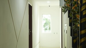 Een gang met een deur naar een kamer, een raam met uitzicht op groen en een muur met een decoratief patroon.