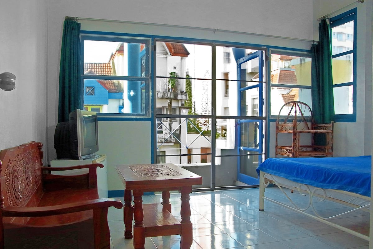 Una habitación con una cama, una mesa de madera, un televisor y una ventana con vistas a edificios.