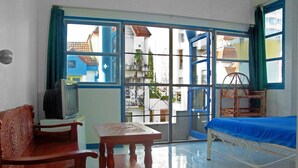 A room with a bed, a wooden table, a television, and a window with a view of buildings outside.