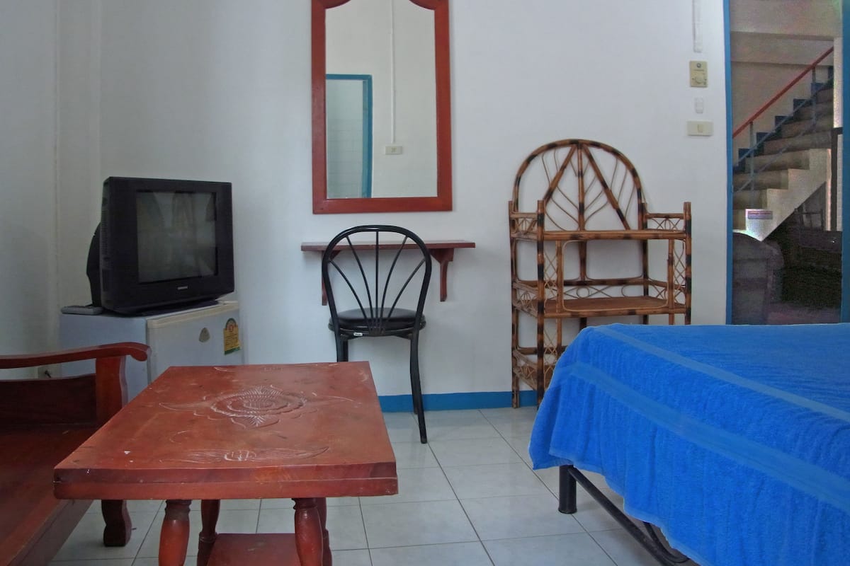Una habitación con cama, mesa, silla, televisor, espejo y escalera.