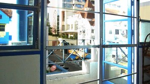 A view through a glass door with a metal frame, leading to a balcony with a tiled floor.