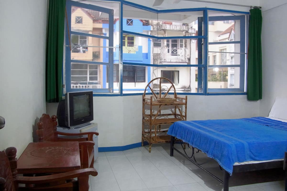 Una habitación con cama, televisión, silla y ventana con vistas a edificios.