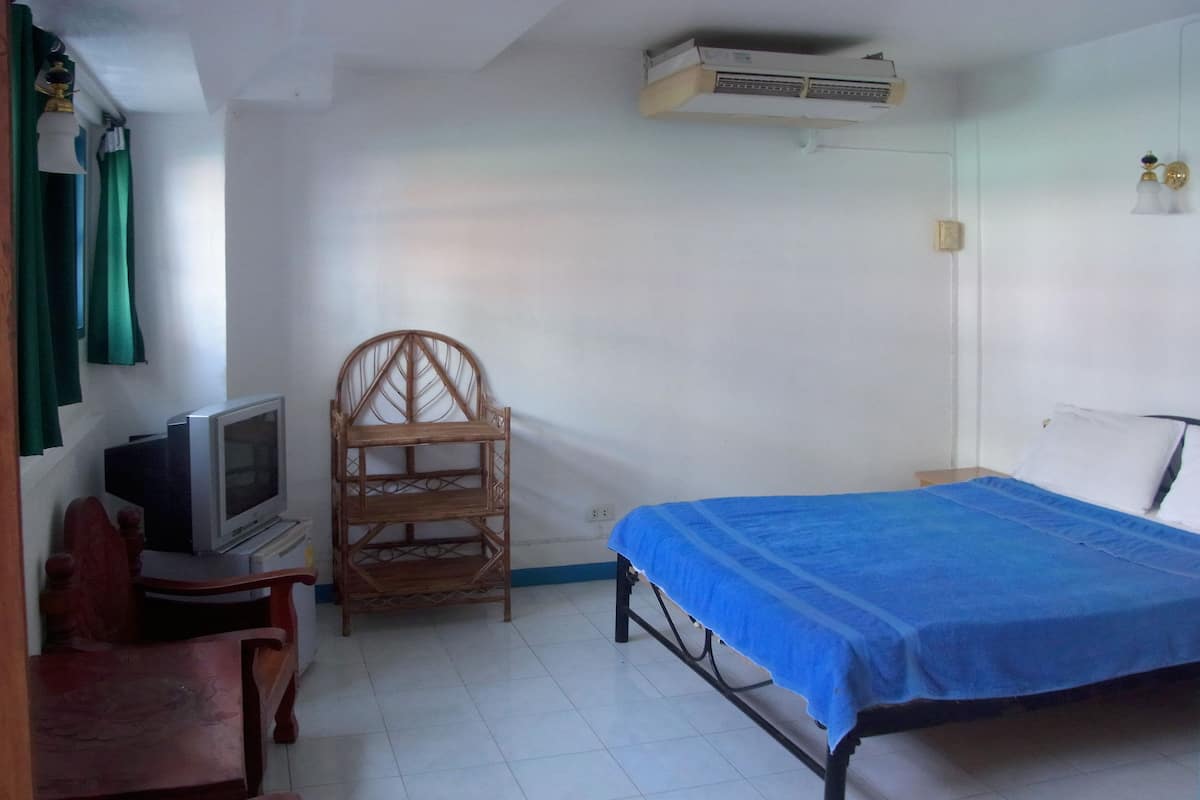 Un dormitorio con una cama, un televisor, una silla de madera y un aire acondicionado instalado en la pared.