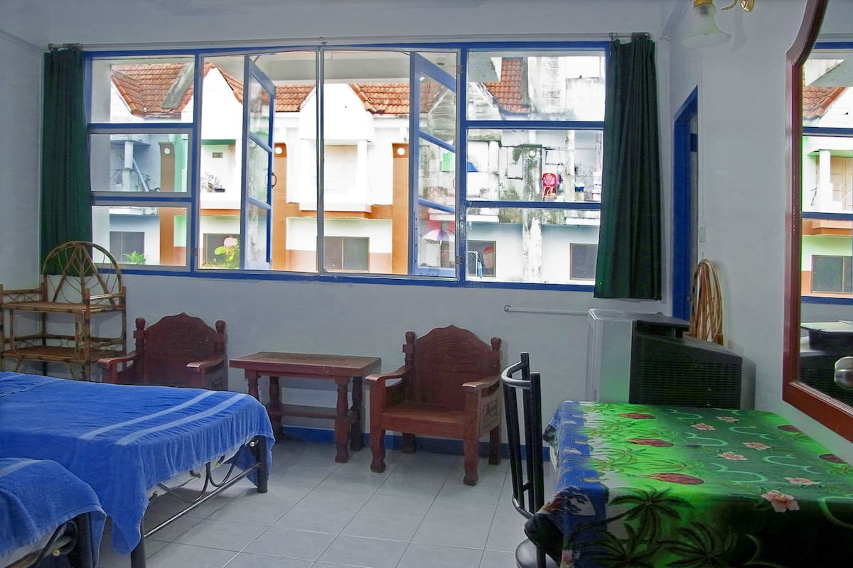 Una habitación con cama, dos sillas, una mesa y ventana con vista a edificios.