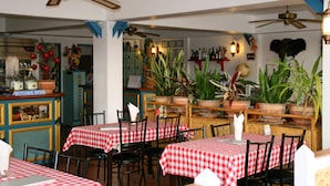 A restaurant with checkered tablecloths, wooden chairs, ceiling fans, and potted plants.