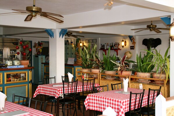 A restaurant with checkered tablecloths, wooden chairs, ceiling fans, and potted plants.