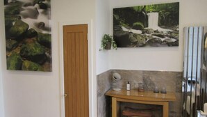 A bathroom with a wooden door, a mirror, a small wooden table with toiletries, and two framed nature paintings on the wall. - Middleton House (Auchterarder)