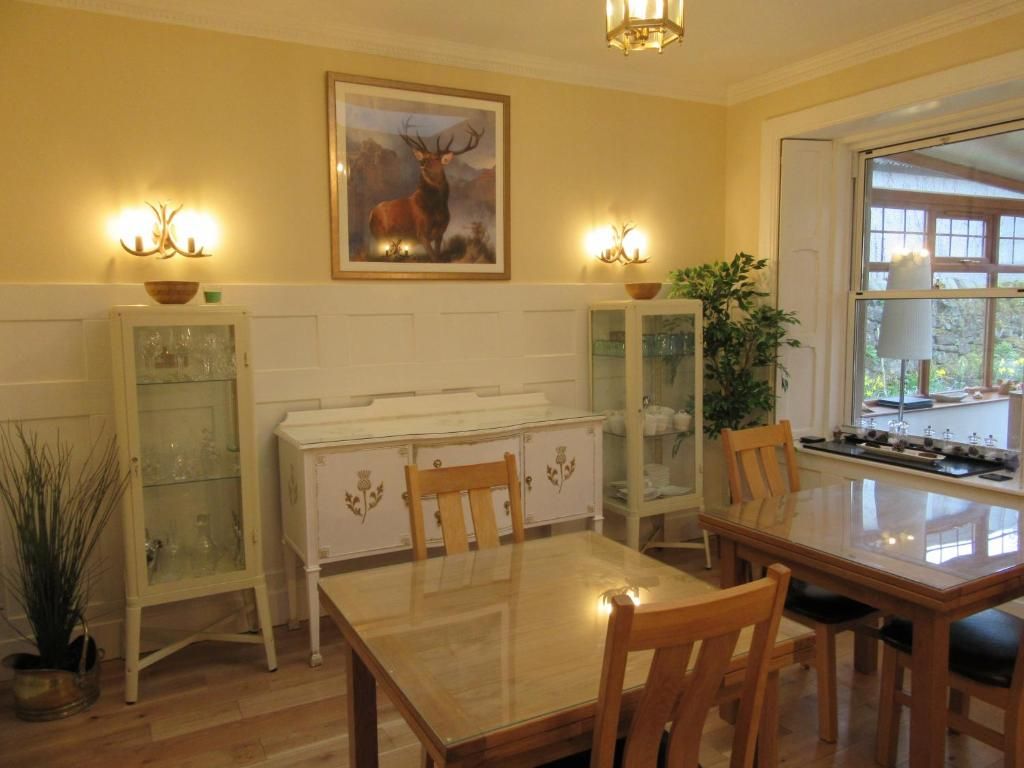 A dining area with a wooden table and chairs, a painting of a deer on the wall, and a window with a view of greenery.