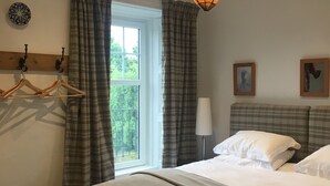 A hotel room with a bed, a chair with deer print upholstery, a hanging light fixture, a window with curtains, and a wall-mounted coat rack. - Middleton House (Auchterarder)