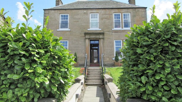 A stone building with a central entrance, flanked by symmetrical hedges, and a clear sky above. - Middleton House (Auchterarder)