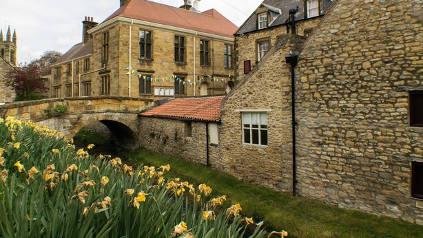 A stone building with a red-tiled roof, a stone archway, and a garden with yellow flowers. - The Royal Oak Hotel (York)